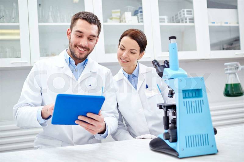 Science, chemistry, technology, biology and people concept - young scientists with tablet pc and microscope making test or research in clinical laboratory, stock photo