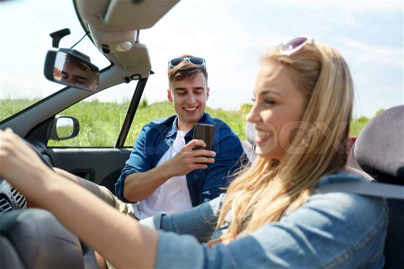 Leisure, road trip, travel, summer holidays and people concept - happy couple driving in cabriolet car and taking picture by smartphone, stock photo