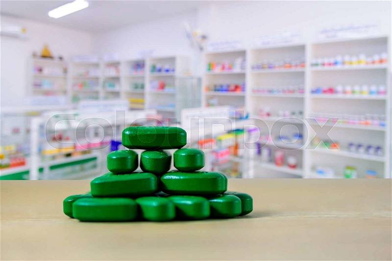 Green pills on wooden table with blurred pharmacy interior, stock photo