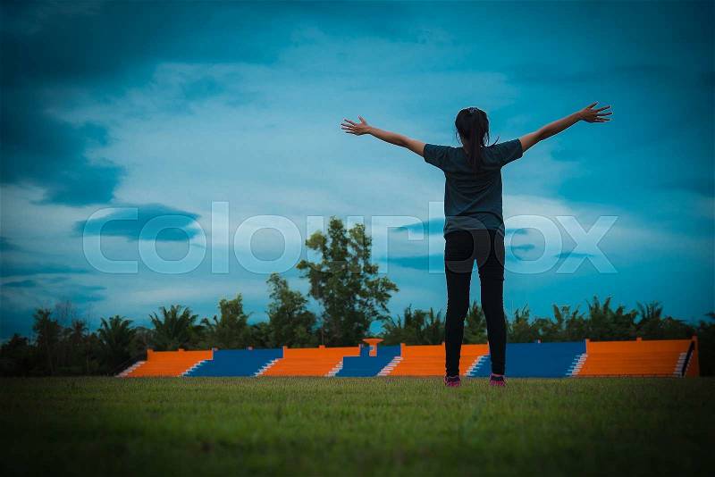 Woman pulls hands to the sky on green grass in stadium. Vintage tone, stock photo