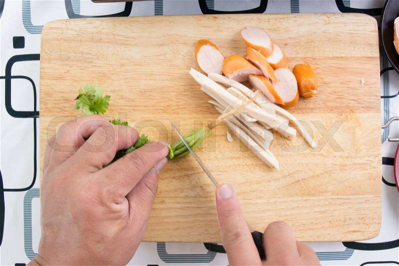 Chef chops coriander with knife beside slice of sausage / Cooking egg pan concept, stock photo