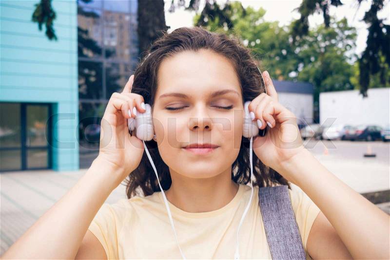 Cute girl listening to music on headphones with eyes closed in the city, stock photo