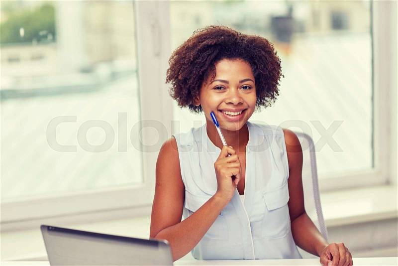 Education, business and technology concept - happy african american businesswoman or student with laptop computer and pen at office, stock photo