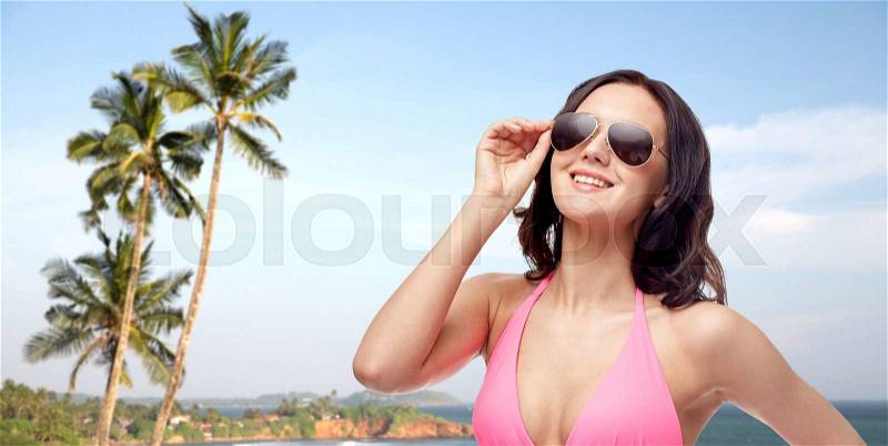 People, fashion, summer and travel concept - happy young woman in sunglasses and pink bikini swimsuit over Sri Lanka beach with palms background, stock photo