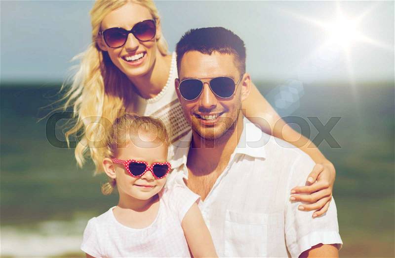 Family, vacation, adoption and people concept - happy man, woman and little girl in sunglasses on summer beach, stock photo