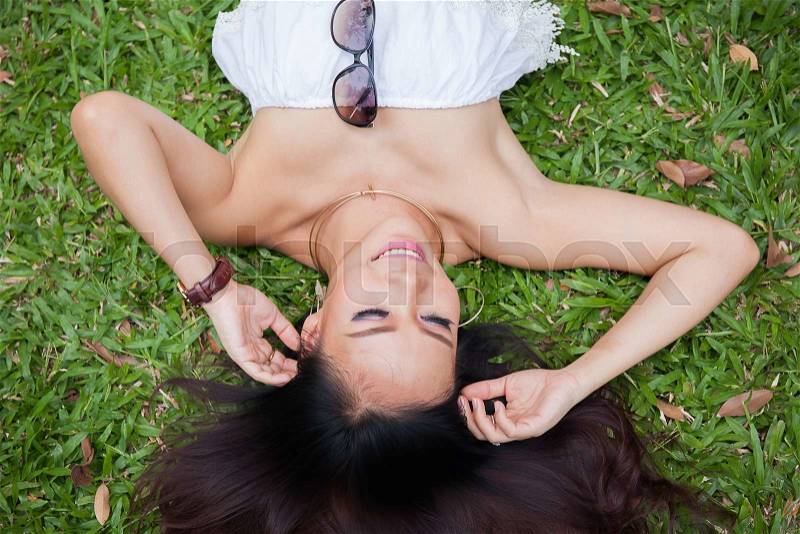Young happy and smiling woman laying down on green grass - happiness concept, stock photo