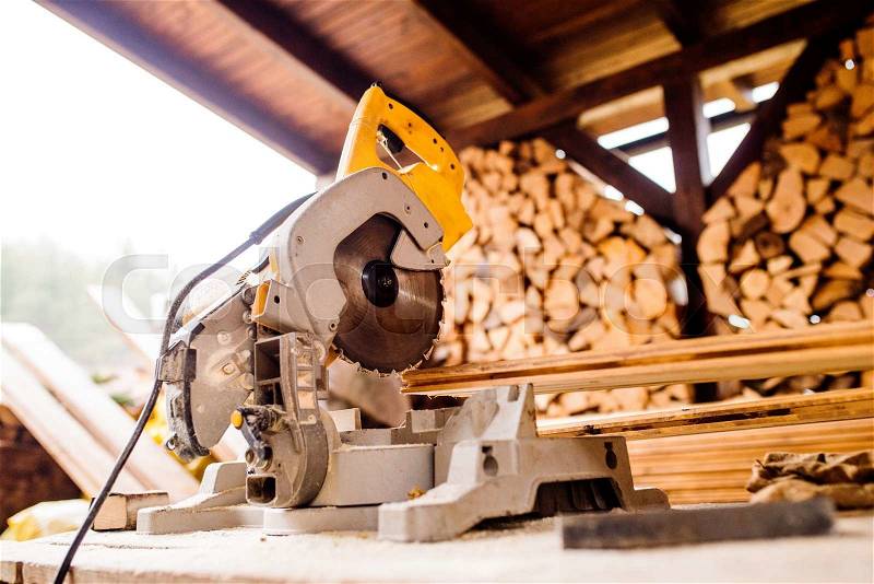 Close up of circular saw laid on table, stack of wood behind it, stock photo