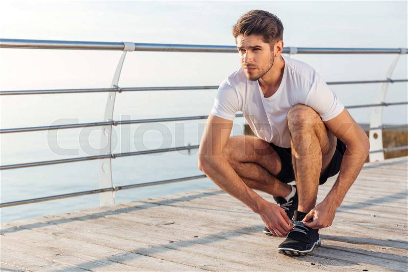 Closeup of man athlete laces his sneakers on pier, stock photo