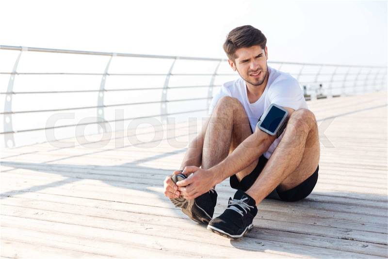Exhausted young sportsman tired after running sitting at the pier outdoors, stock photo