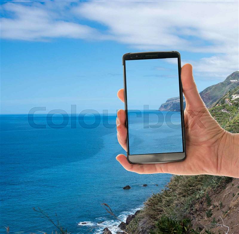 Female hand with mobile phone showing the coast of madeira island, stock photo