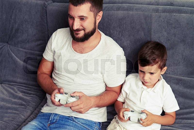 Small boy is willing to win while playing a videogame with his dad using joysticks , stock photo
