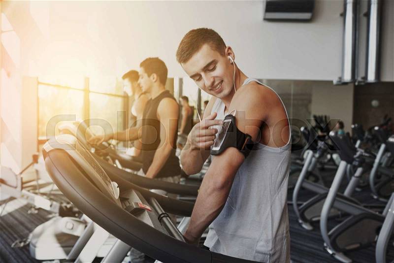 Sport, fitness, lifestyle, technology and people concept - man with smartphone and earphones exercising on treadmill in gym, stock photo