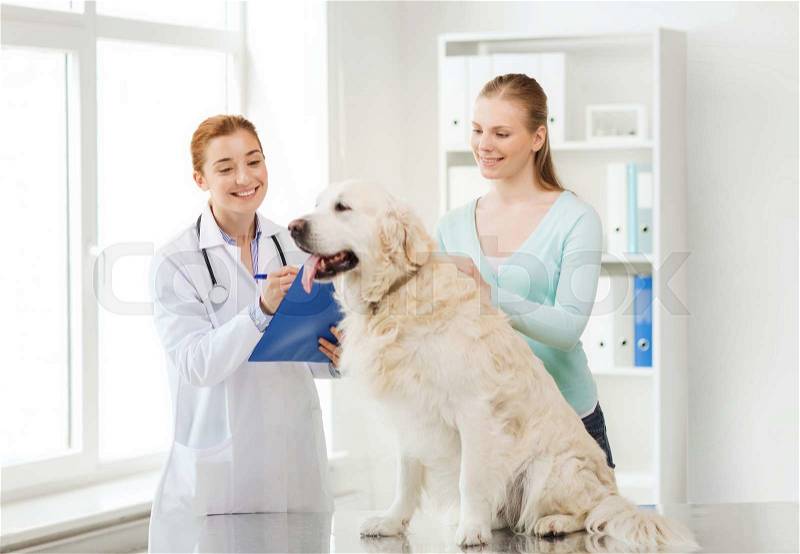 Medicine, pet, animals, health care and people concept - happy woman with golden retriever dog and veterinarian doctor writing to clipboard at vet clinic, stock photo