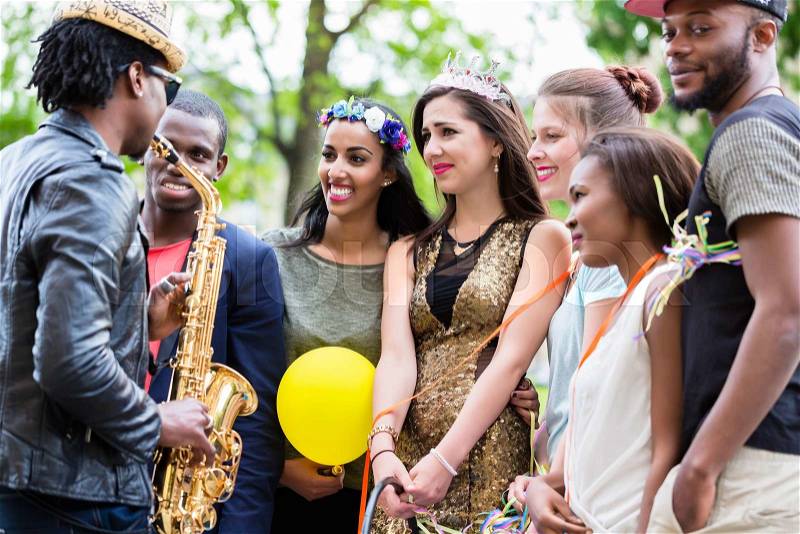 Street artist playing saxophone for a multi-ethnic party group of young women on a hens night, stock photo