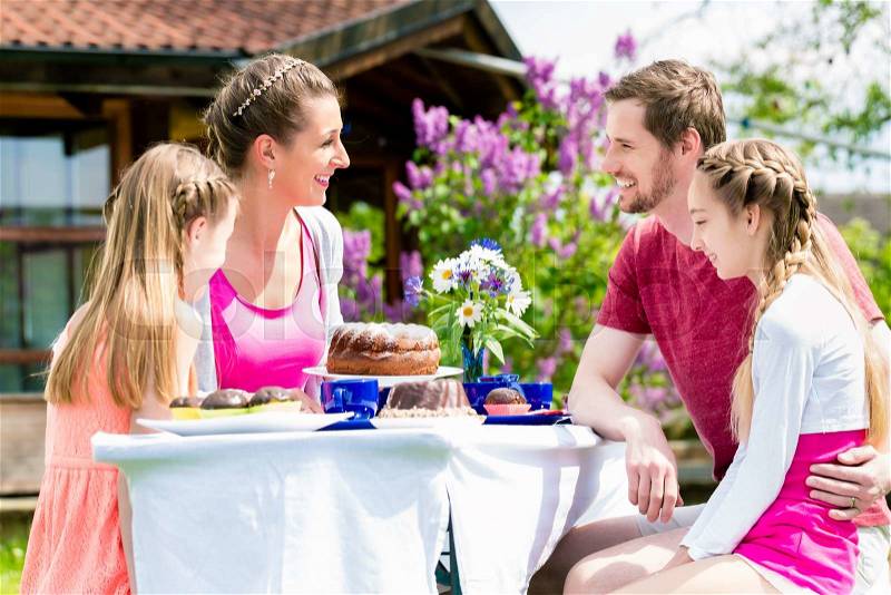 Family having coffee and cake in garden at house, stock photo