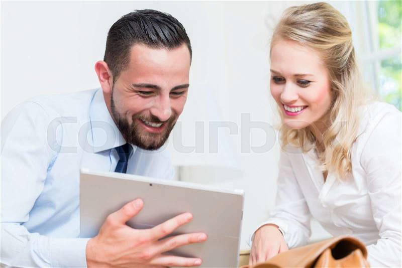 Business woman and man in work meeting looking at presentation on tablet computer, stock photo