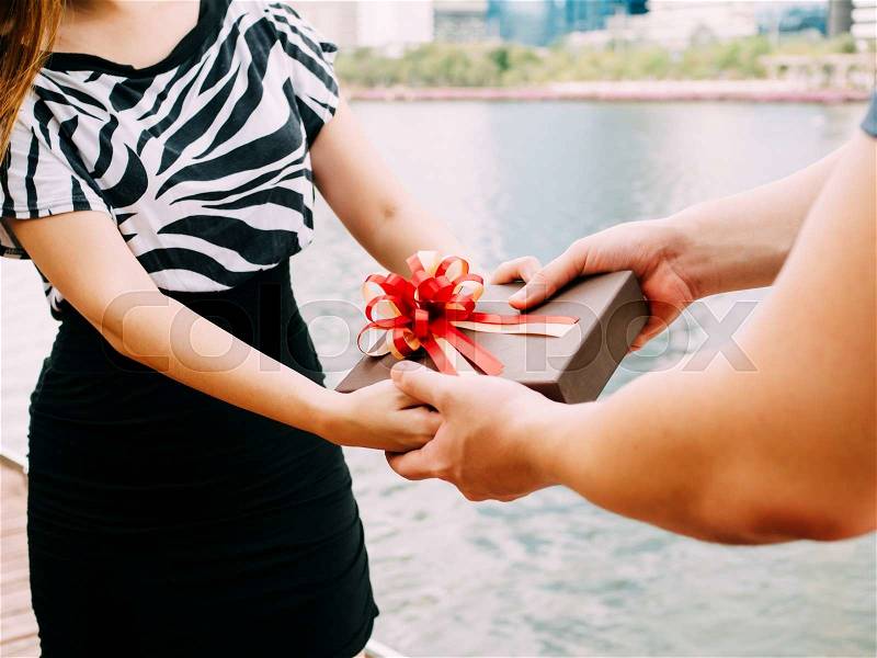 Couple giving a gift box to each other. Happy relationship in outdoor scene. Love and relationship concept, stock photo