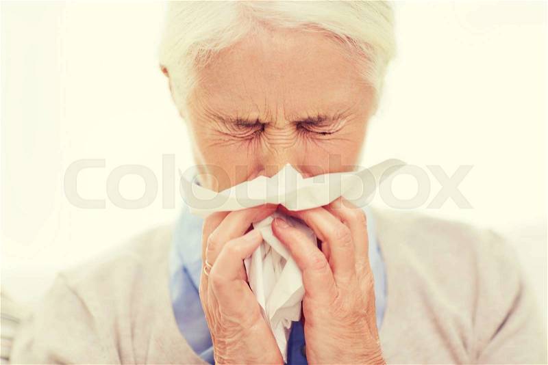 Health care, flu, hygiene, age and people concept - sick senior woman blowing nose to paper napkin at home, stock photo