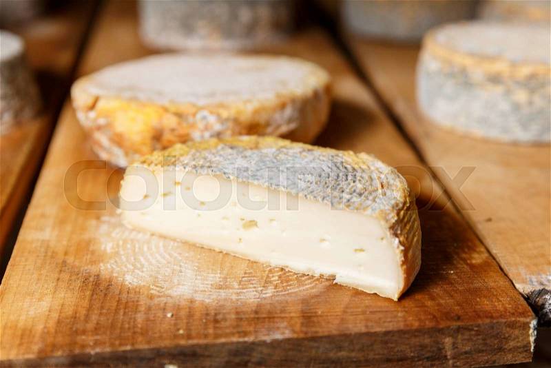Piese of young and soft goat cheese head with a blue mold on a wooden shelf in a cellar on a private farm. Cheese manufacture, stock photo