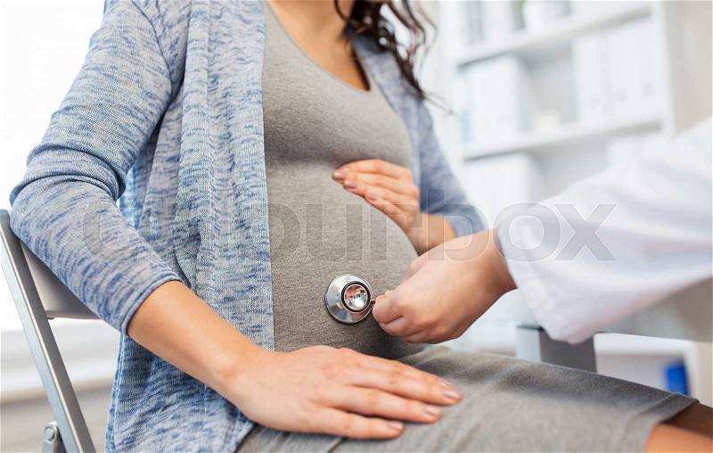 Pregnancy, gynecology, medicine, health care and people concept - close up of gynecologist doctor with stethoscope listening to pregnant woman baby heartbeat at hospital, stock photo