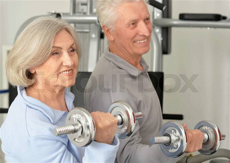 Active smiling senior couple exercising in gym, stock photo
