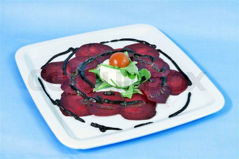 Modern food on a white plate and blue background - Thin slices of beetroot with goat cheese and balsamic reduction, stock photo