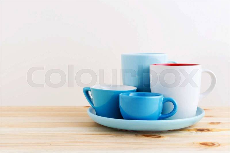 Blue cups and white mug on plate on wooden table with space, stock photo