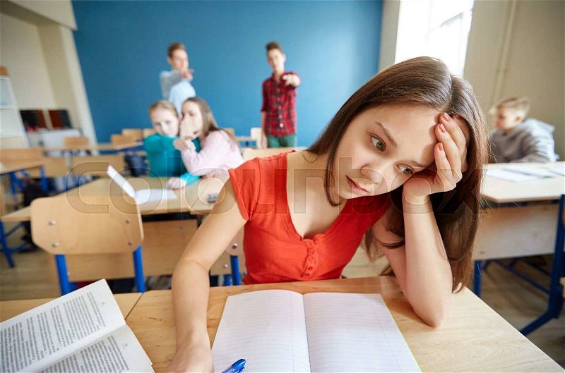 Education, bullying, conflict, social relations and people concept - students teasing and judging girl classmate behind her back at school, stock photo