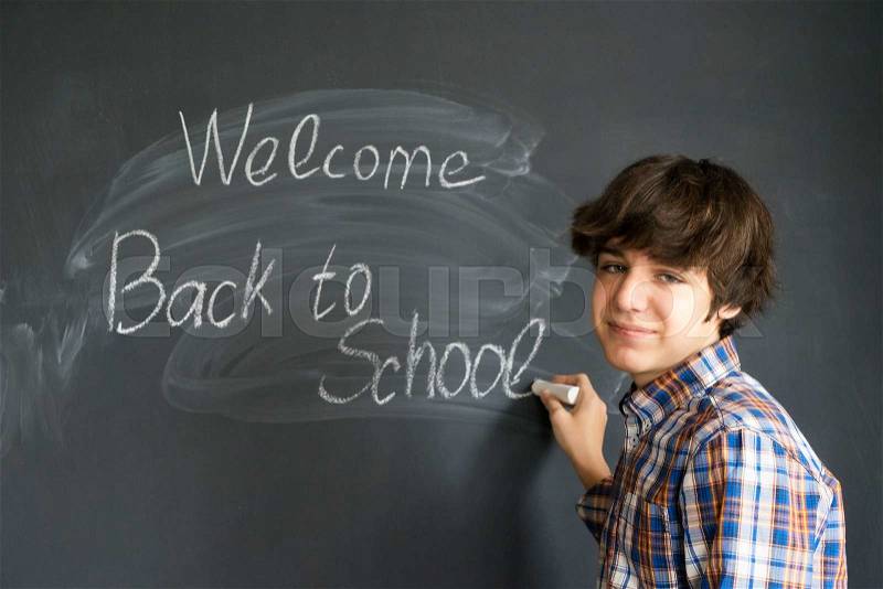 Boy writting back to school on black board background, stock photo