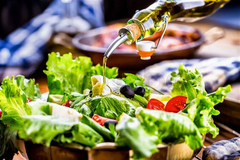Vegetable lettuce salad. Olive oil pouring into bowl of salad. Italian Mediterranean or Greek cuisine. Vegetarian vegan food, stock photo