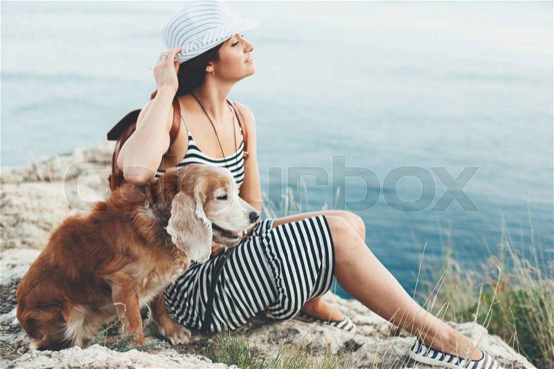 Woman hugs with her dog sitting on mountain over sea view, stock photo