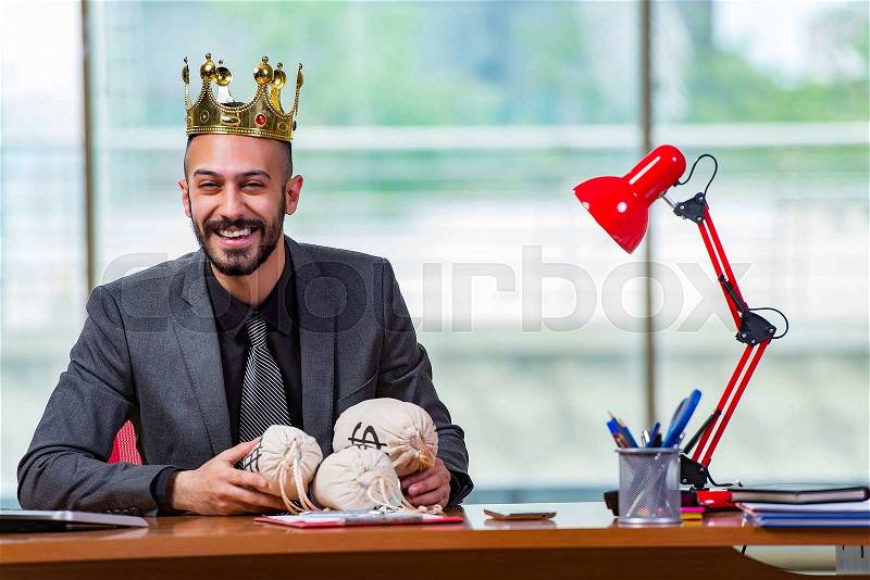 Businessman with crown and money sacks in the office, stock photo