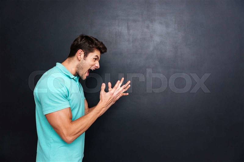 Side view of a angry casual young man screaming isolated over black chalkboard, stock photo