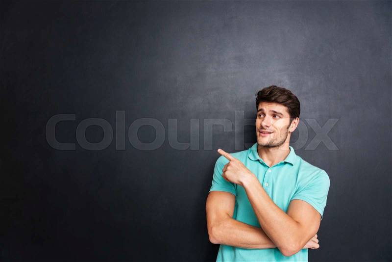 Portrait of a casual young handsome man pointing away and leaning on the black chalk blackboard, stock photo