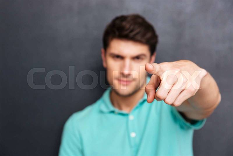 Close up portrait of a handsome man pointing finger at camera isolated on a black chalkboard, focus on finger, stock photo