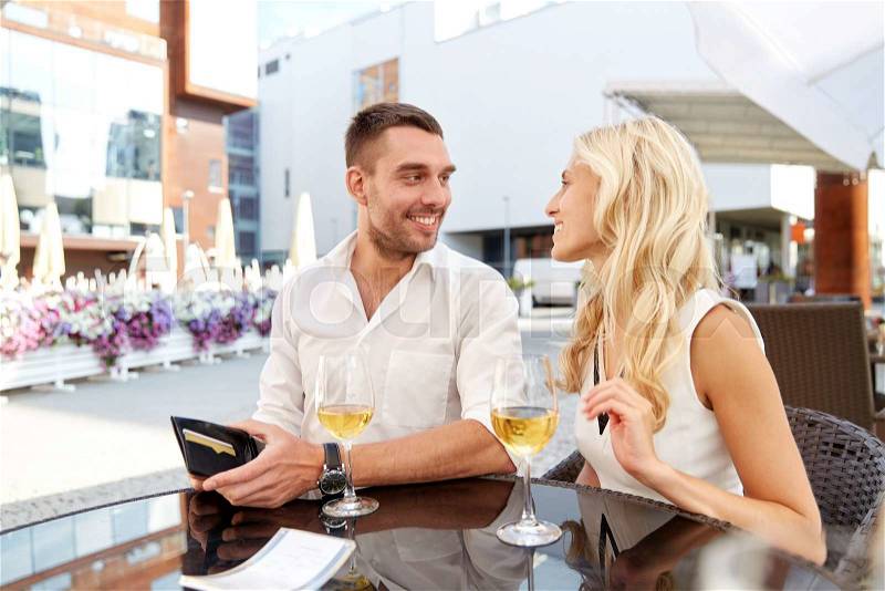 Date, people, payment and finances concept - happy couple with wallet and wine glasses paying bill at restaurant, stock photo