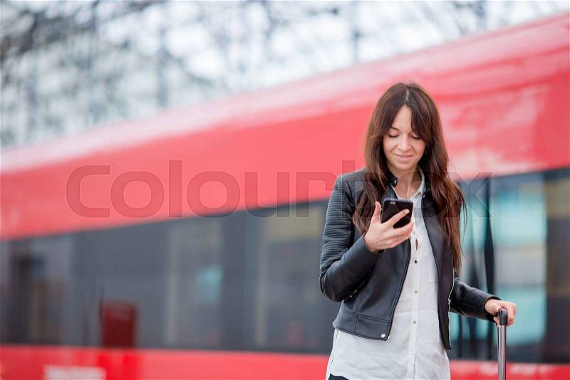 Young woman with luggage looking oh cellphone at a train station. Caucasiam tourist waiting her express train while her traveling, stock photo