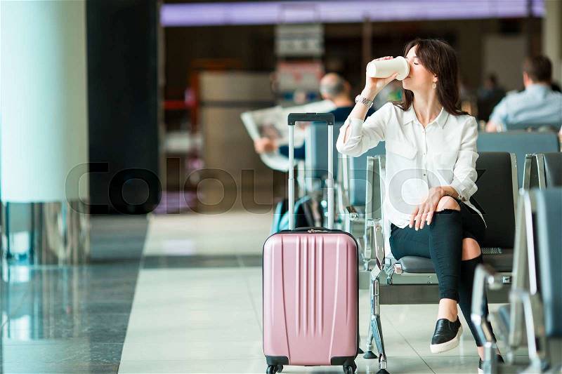 Airline passenger in an airport lounge drinking coffee and waiting for flight aircraft. Caucasian woman with glasss if hot coffee in the waiting room, stock photo
