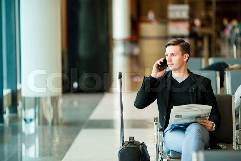 Urban business man talking on smart phone inside in airport. Casual young businessman wearing suit jacket. Handsome male model. Young man with cellphone at the airport while waiting for boarding, stock photo