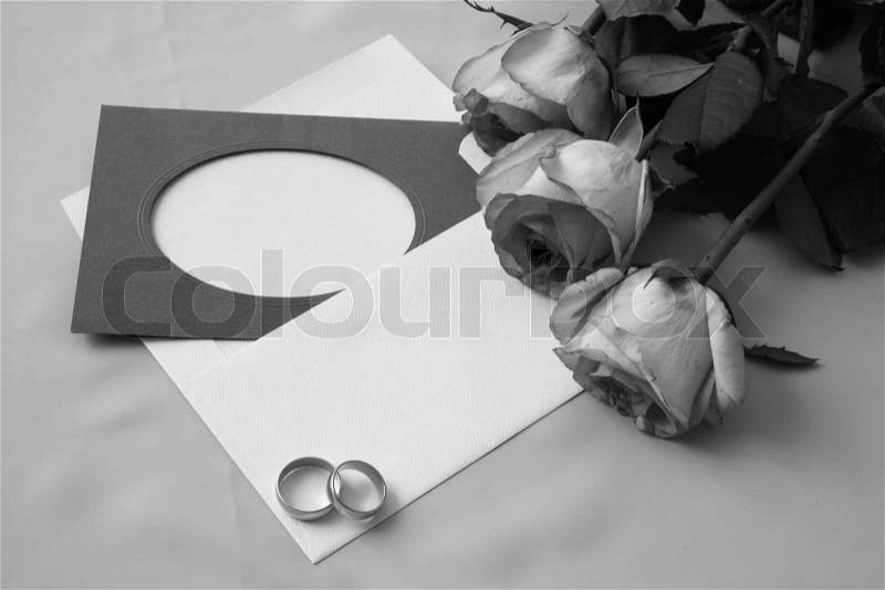 On a photo a card, an envelope, roses and gold rings. A black-and-white photo, stock photo