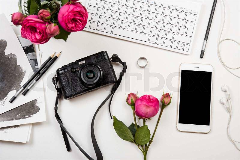 Modern smartphone, computer keyboard, pink flowers and photo camera on white table, freelancer girl\'s workspace, stock photo