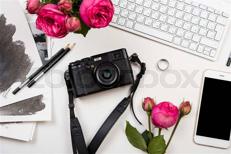 Modern smartphone, computer keyboard, pink flowers and photo camera on white table, freelancer girl\'s workspace, stock photo