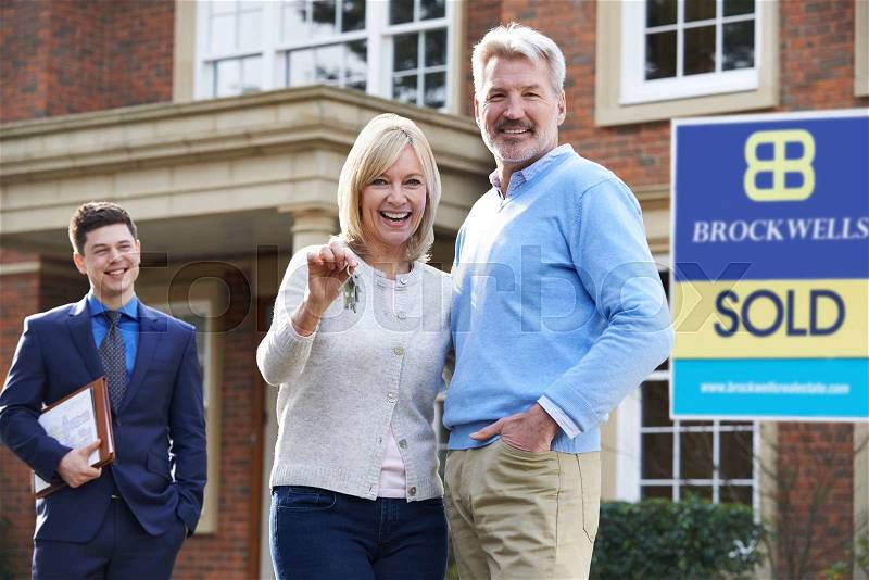 Mature Couple Collecting Keys To New Home From Realtor, stock photo