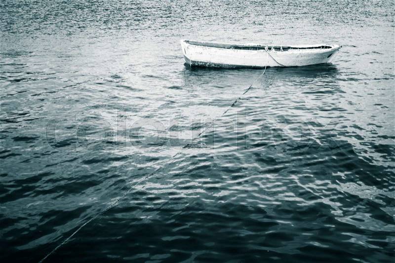 White wooden fishing boat floats on still Sea, blue toned vintage stylized photo, stock photo
