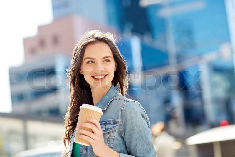 Drinks and people concept - happy young woman or teenage girl drinking coffee from paper cup on city street, stock photo