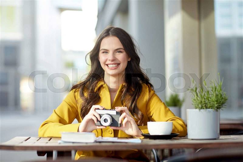 Travel, tourism, photography, leisure and people concept - happy young tourist woman or teenage girl with film camera and guidebook drinking cocoa at city street cafe terrace, stock photo
