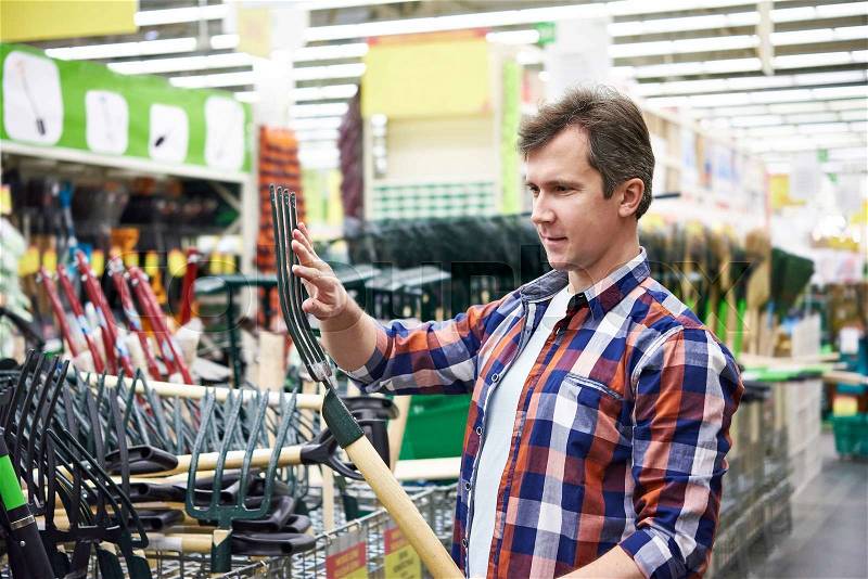Man chooses pitchfork hay in store for working in the garden, stock photo