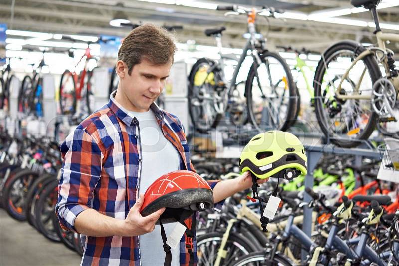 Man chooses helmet for cycling before buying in sports shop, stock photo