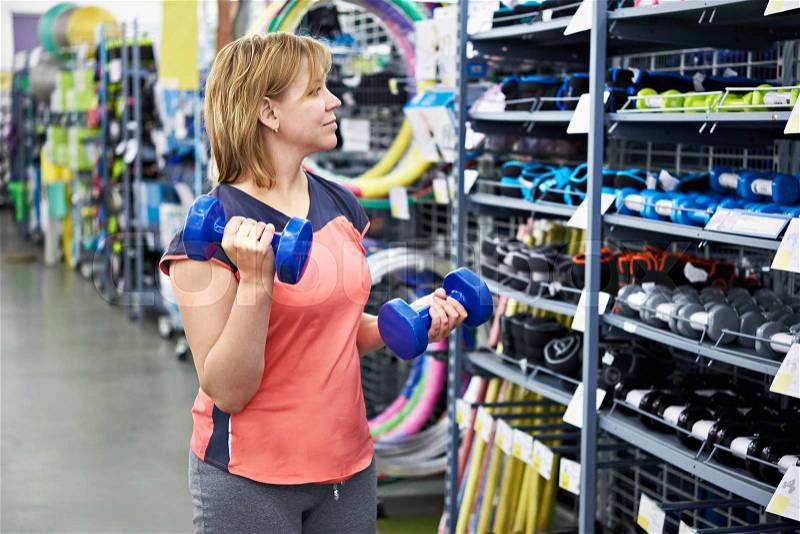 Woman chooses dumbbells for fitness in the sports shop, stock photo