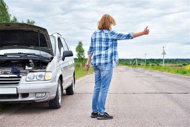 Woman with wrench waiting to help and showing thumbs up near her broken car, stock photo